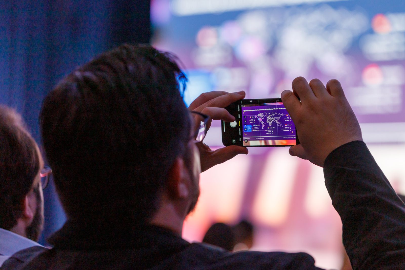 Attendee filming the stage on a phone from the audience