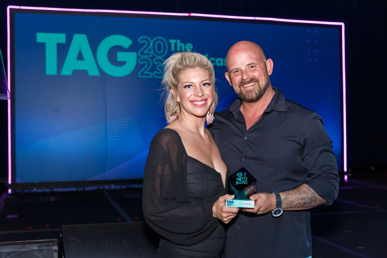 Two award winners posing with a trophy on stage