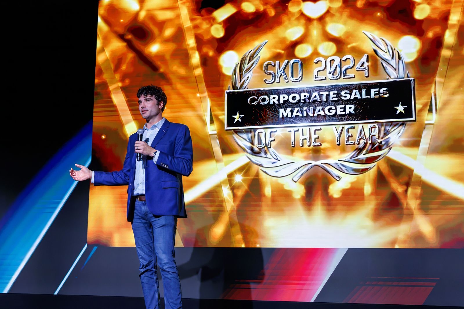 Presenter on stage in front of a gold award graphic