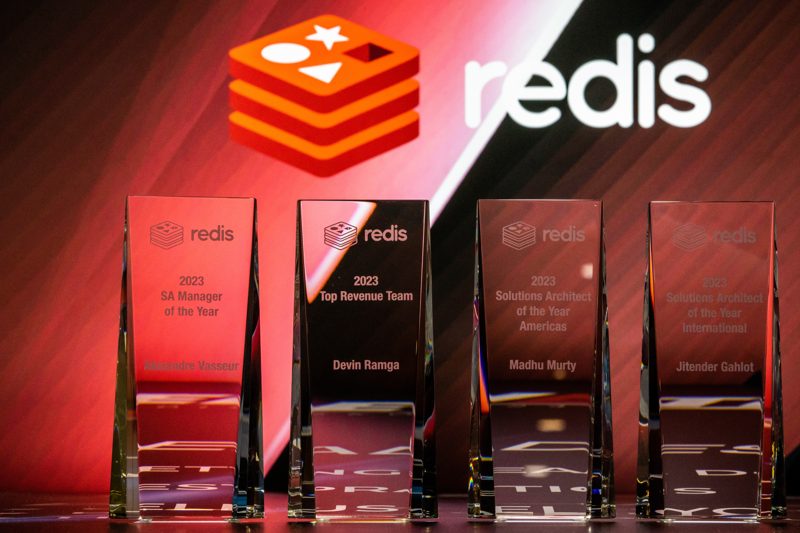 Glass award trophies lined up on stage in front of the sponsor's red branded backdrop