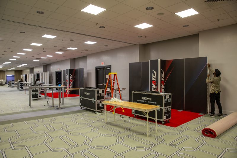 Crew setting up exhibit walls and furniture in an empty hotel ballroom before the event