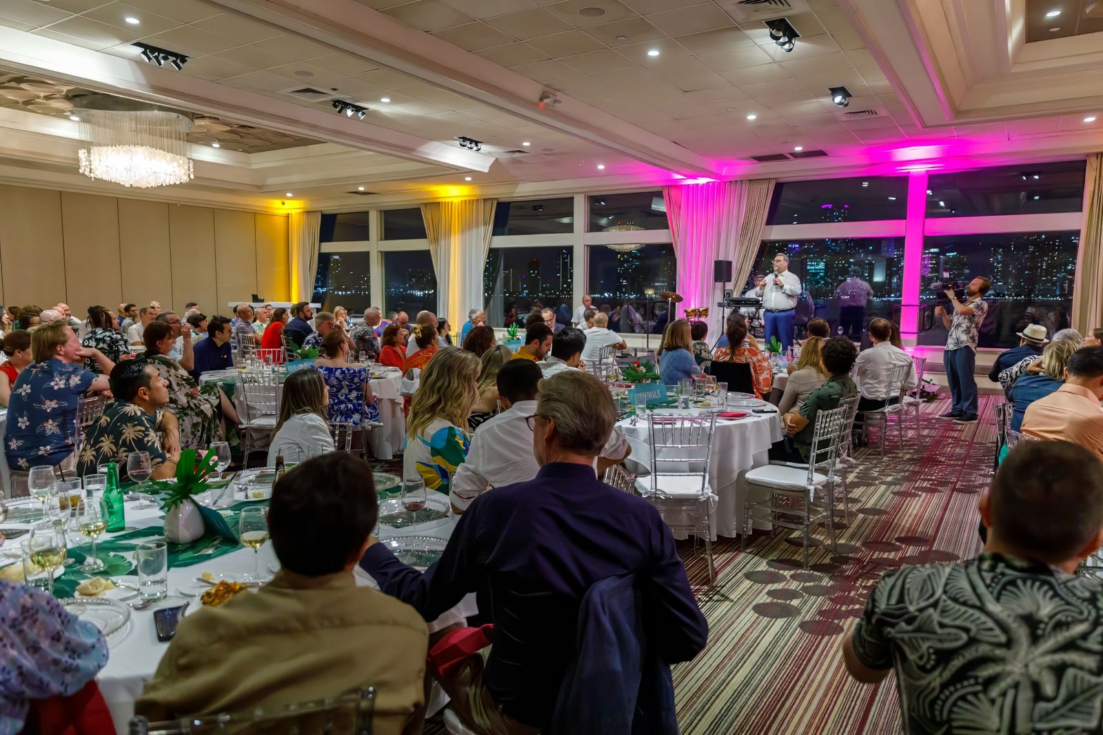 Banquet room full of round tables with pink uplighting