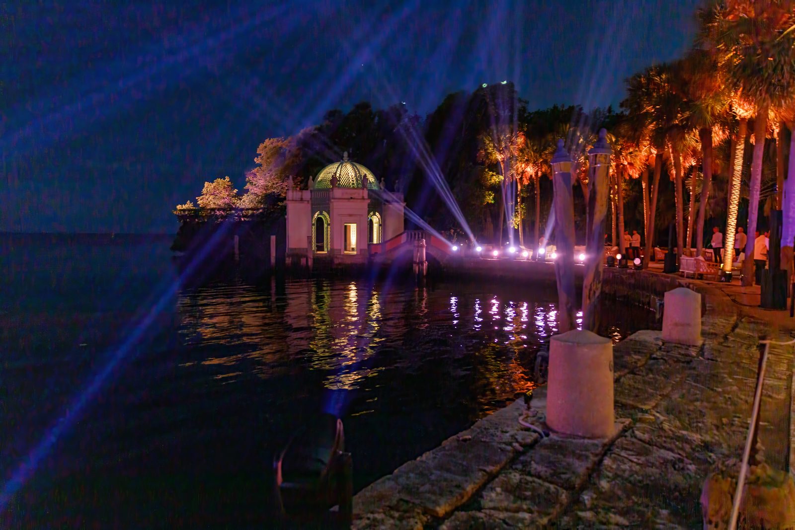 Stone tea house on the bay lit at night with light beams over the water during a gala dinner
