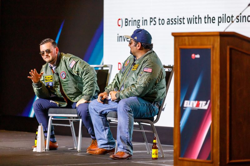 Two presenters in matching flight jackets running a role-play session on stage