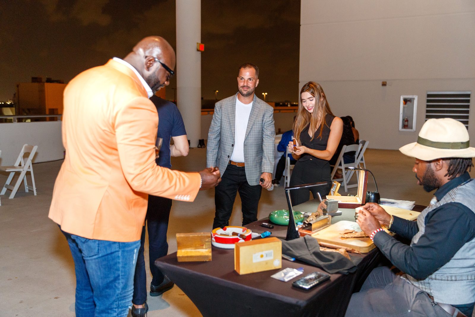Guests gathered around a cigar roller in a Panama hat hand-rolling cigars at a rooftop reception in Miami