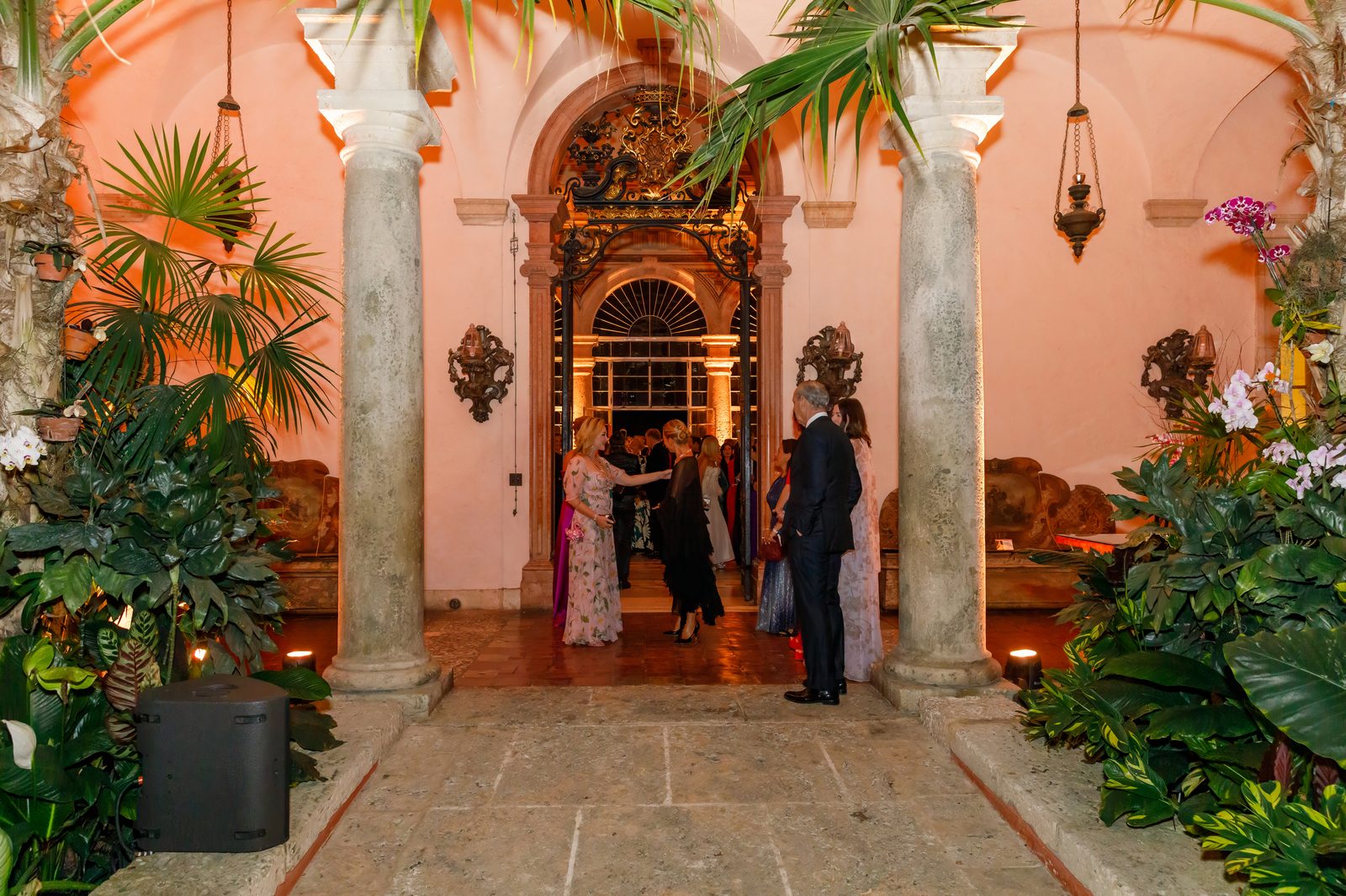 Guests in evening wear arriving through the palm-filled courtyard of Vizcaya's main house in Miami