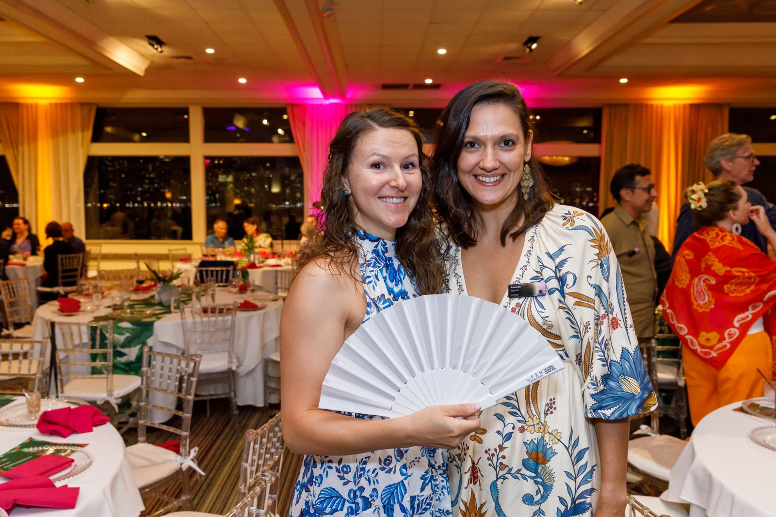 Two guests posing with a hand fan at a themed dinner