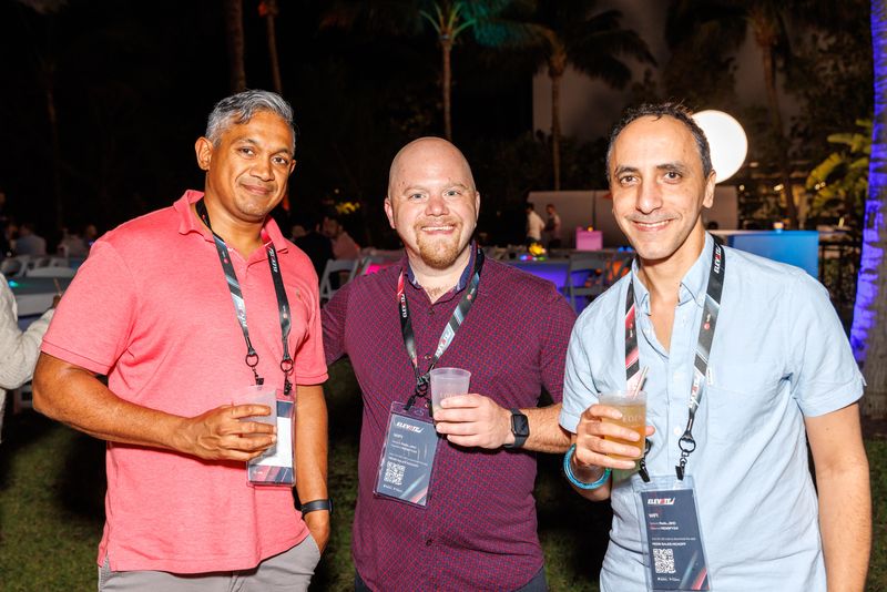 Three attendees with lanyards posing at an outdoor evening party