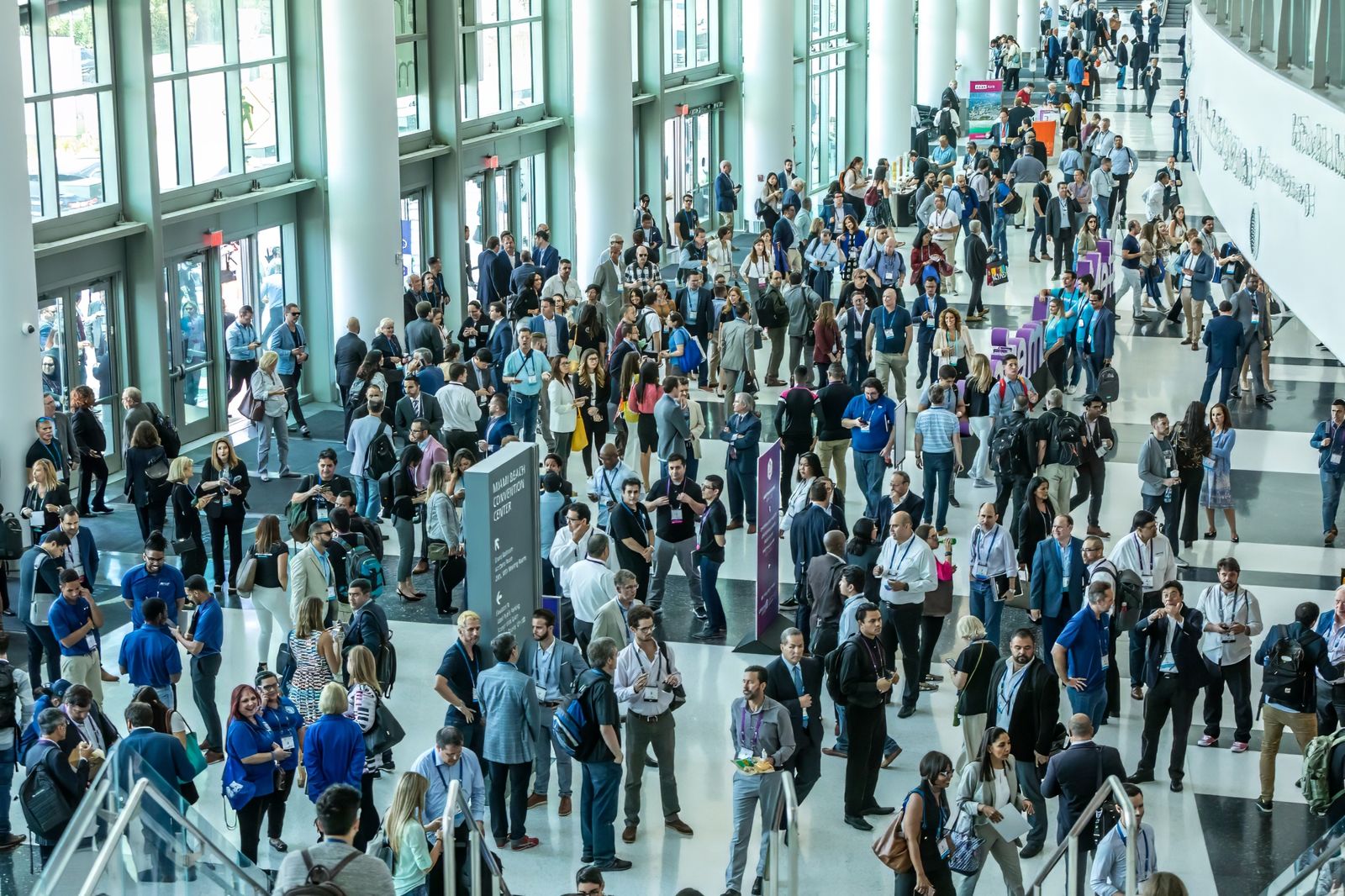 Crowd of attendees with badges filling the glass-walled lobby of the Miami Beach Convention Center during a technology show