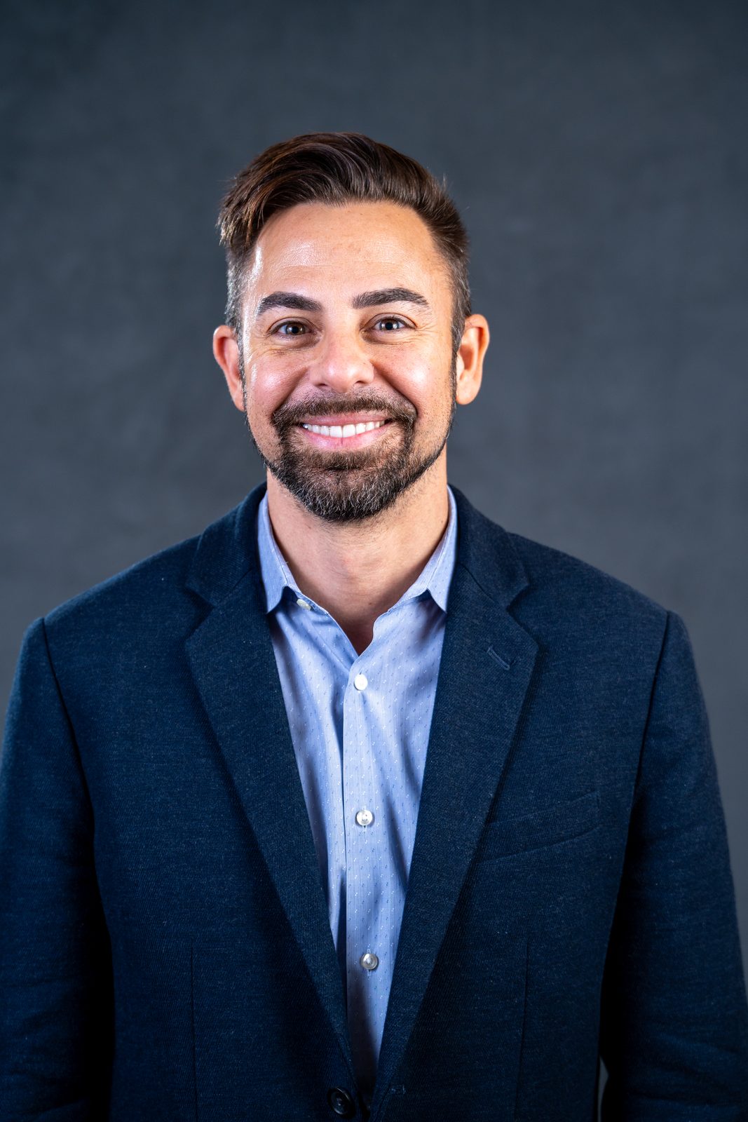 Headshot of a bearded man in a navy blazer against a dark gray backdrop