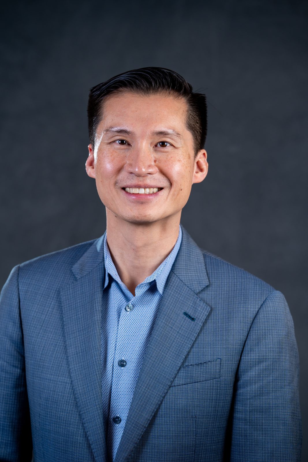 Headshot of a man in a blue blazer against a dark gray backdrop