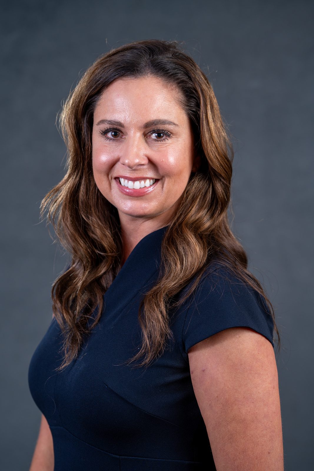 Headshot of a woman in a navy top against a dark gray backdrop