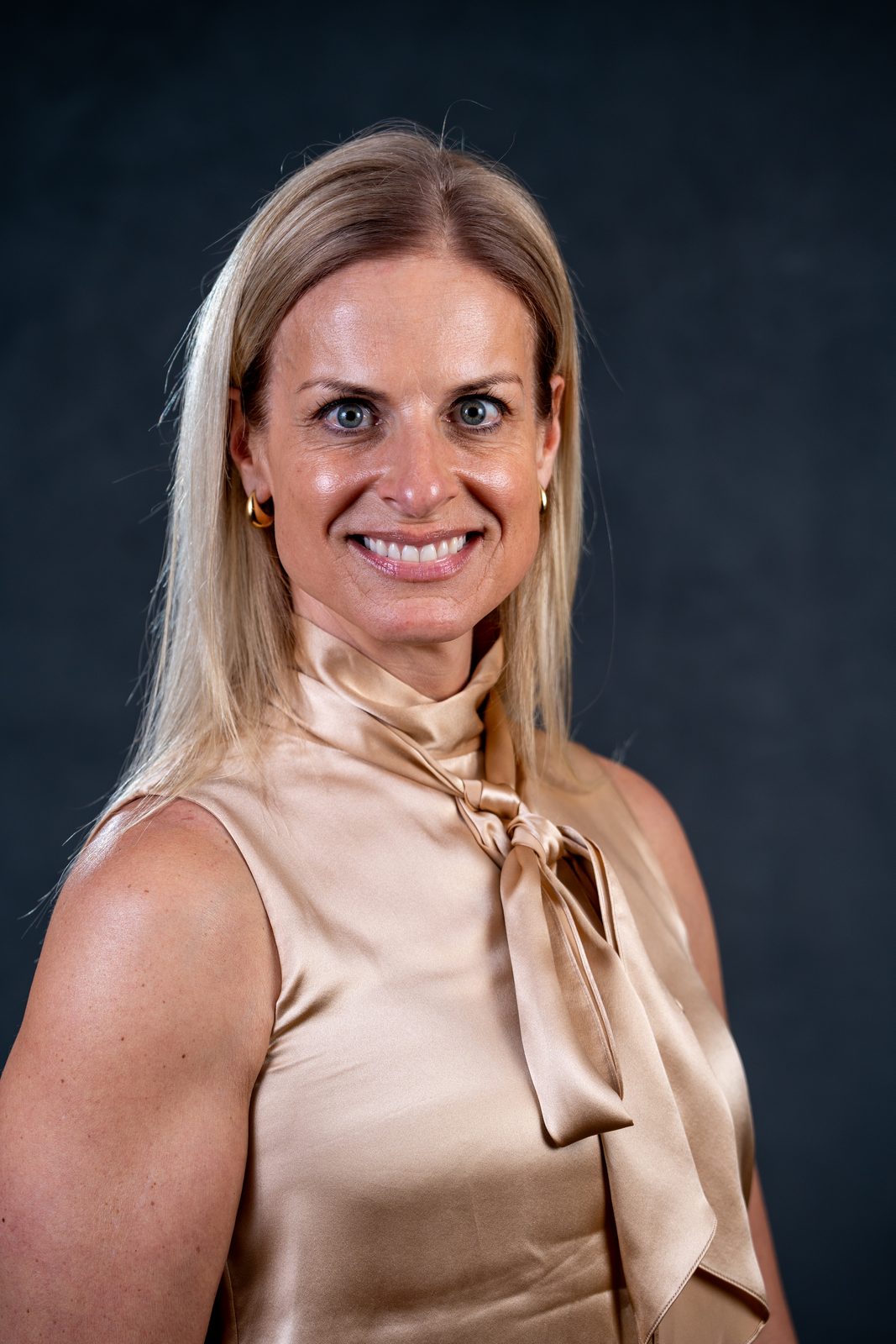 Headshot of a woman in a champagne satin top against a dark gray backdrop