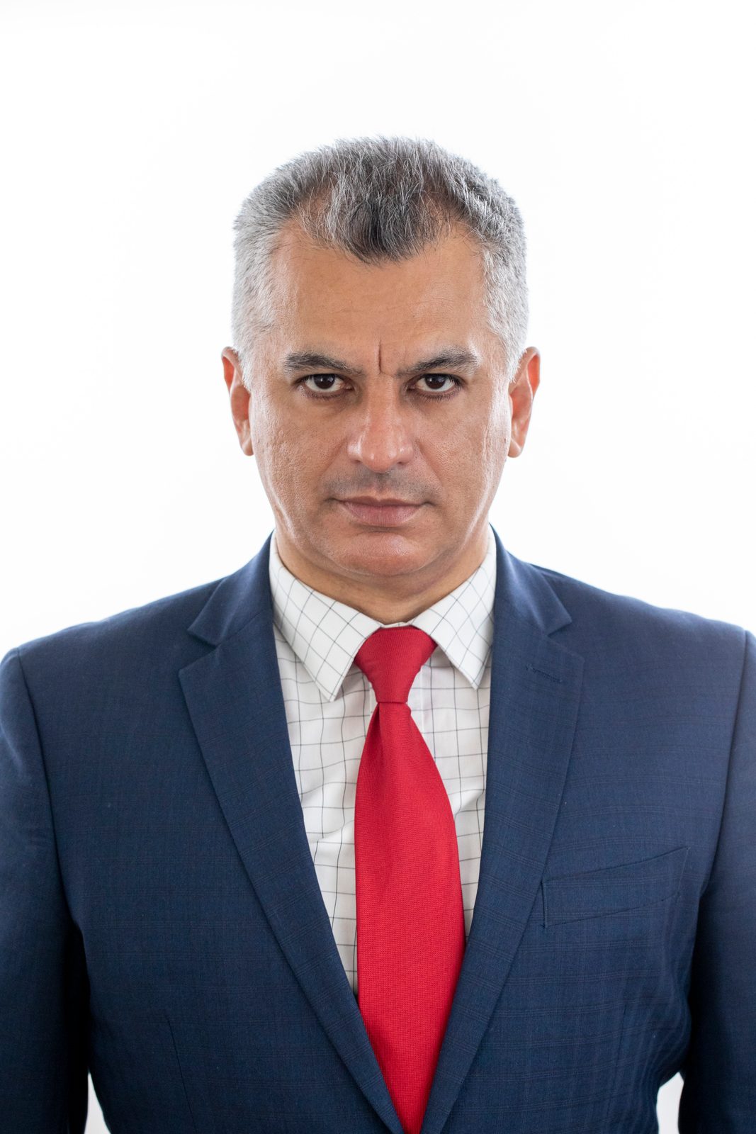 Headshot of a gray-haired man in a navy suit and red tie against a white backdrop