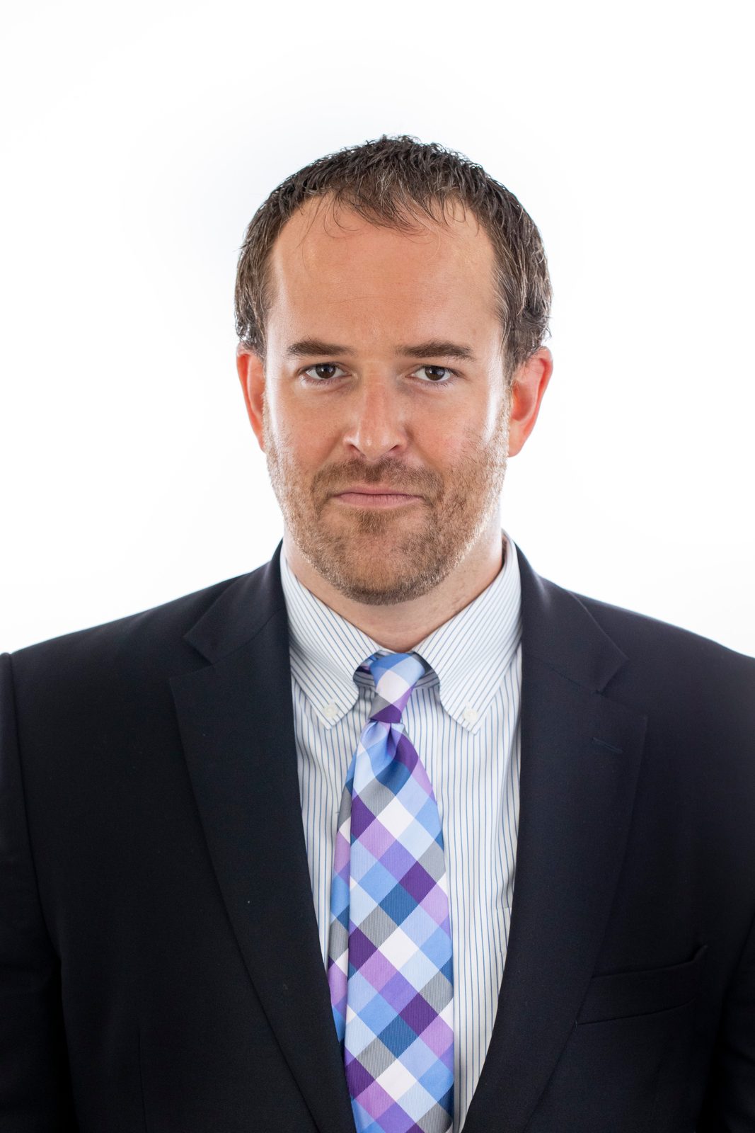 Headshot of a man in a dark suit and checked tie against a white backdrop