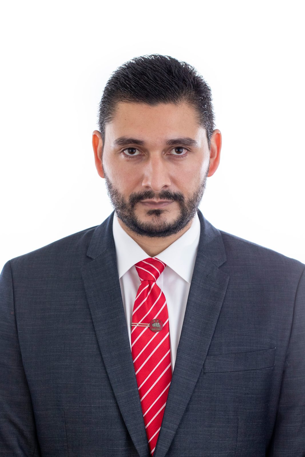 Headshot of a bearded man in a gray suit and red striped tie against a white backdrop