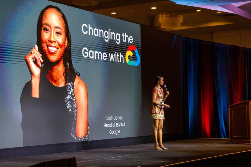 Keynote speaker on a large conference stage in front of a giant screen with her portrait and talk title