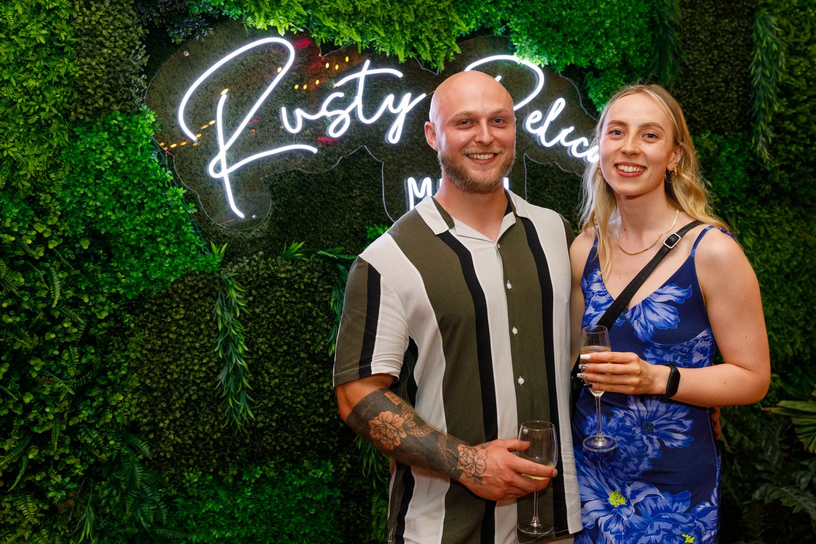Two guests in front of a neon sign on a green wall