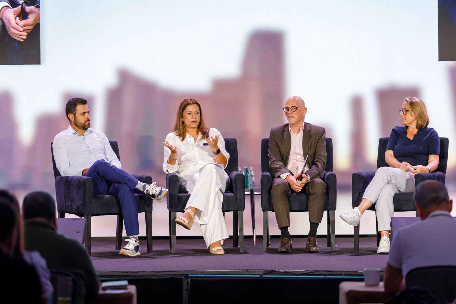 Four panelists in armchairs on a conference stage