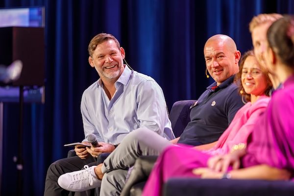Conference panelists laughing together in armchairs on stage