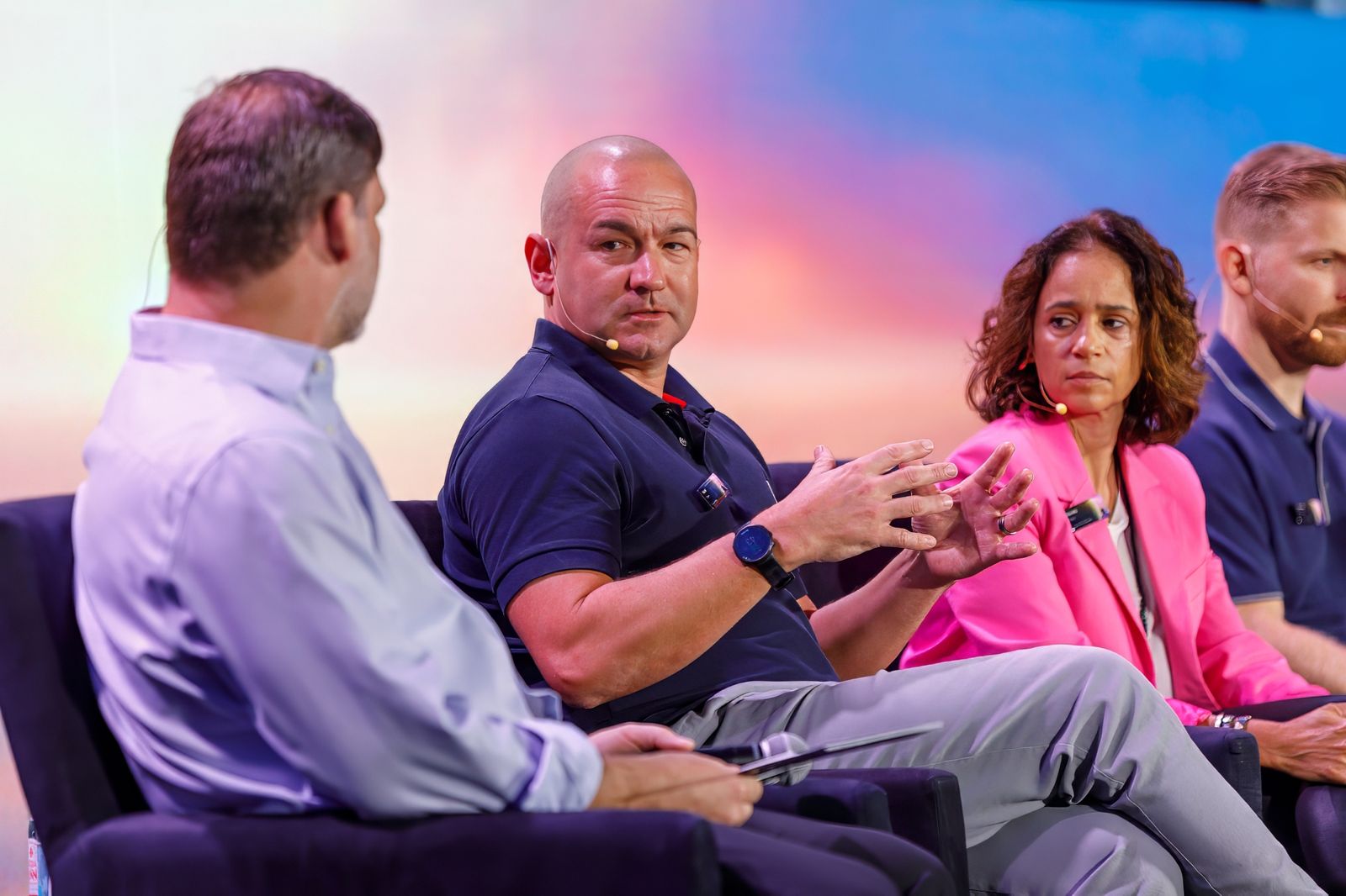 Panelists in armchairs talking on a conference stage in front of a colorful screen