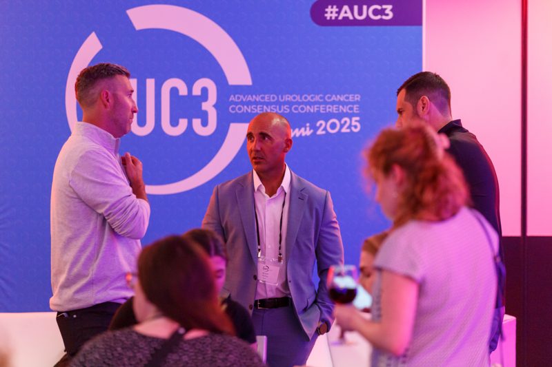 Guests talking with drinks in front of the conference's branded backdrop at the welcome reception