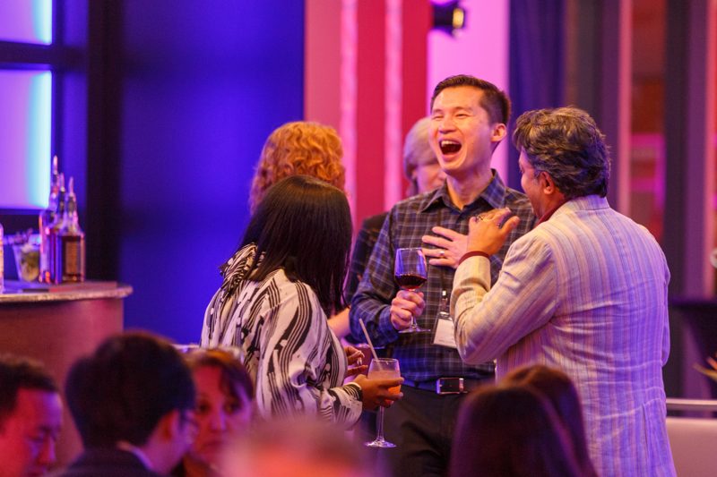 Guests laughing together at an evening welcome reception under purple and red lighting