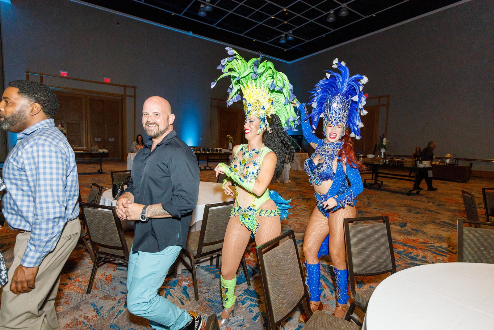 Samba dancers in feathered costumes parading through a ballroom with guests during an evening reception