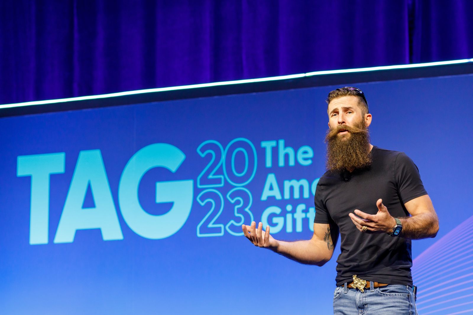 Speaker gesturing on stage in front of a blue event graphic