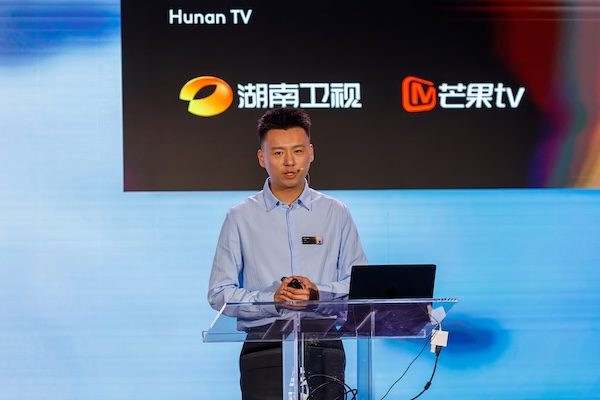 Conference speaker at a clear podium in front of broadcaster logos