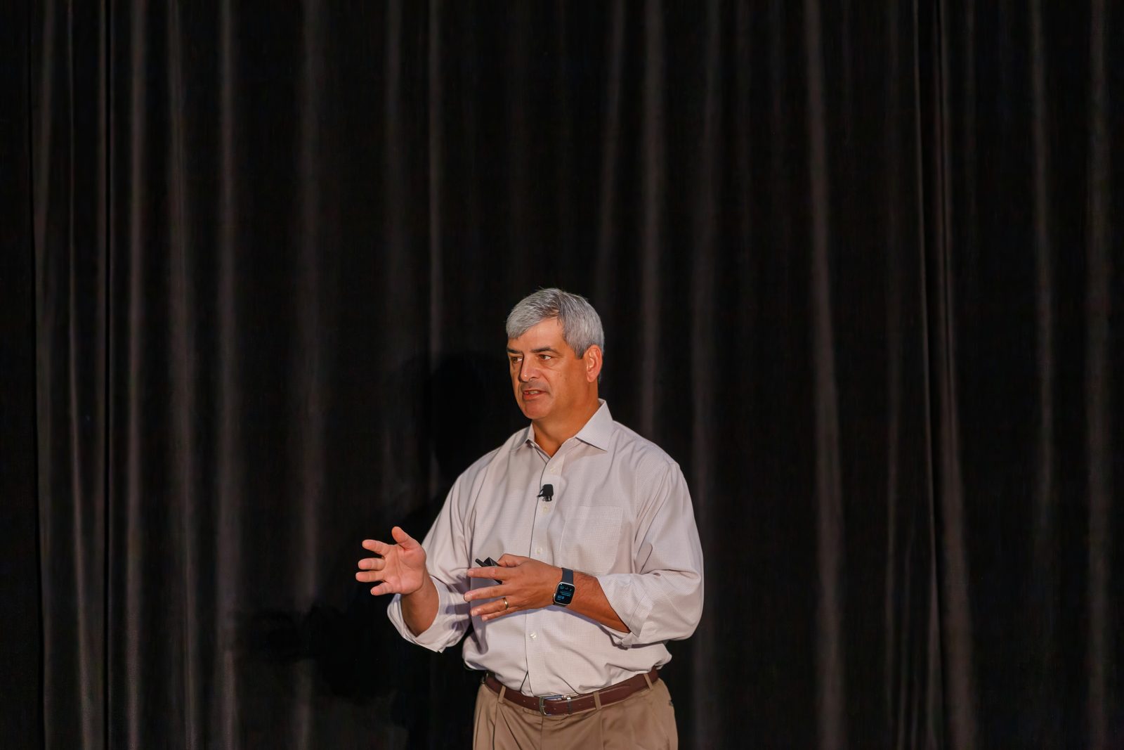 Speaker gesturing mid-talk on a conference stage in front of a dark curtain