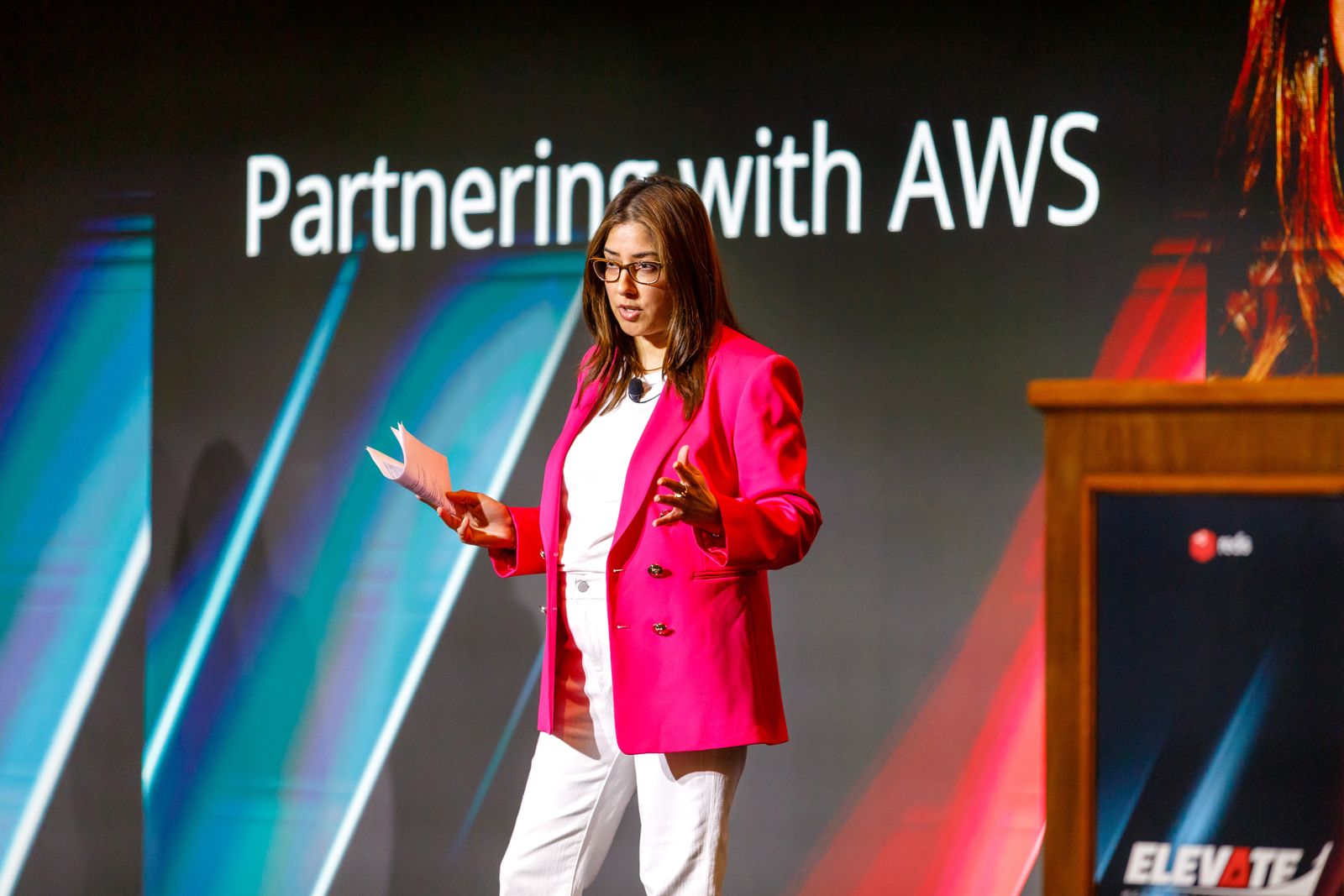 Speaker in a pink blazer presenting on a big stage