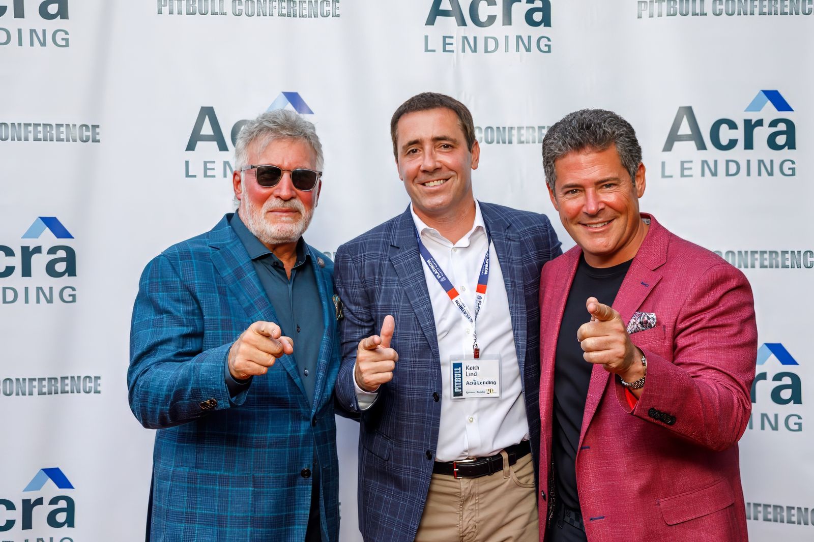 Three guests pointing at the camera in front of a step-and-repeat