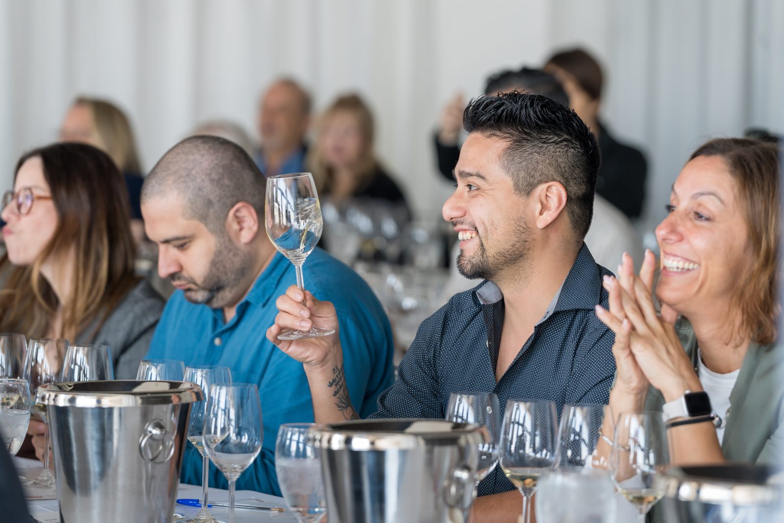 Guests laughing and raising their glasses at a long table during a hosted wine tasting