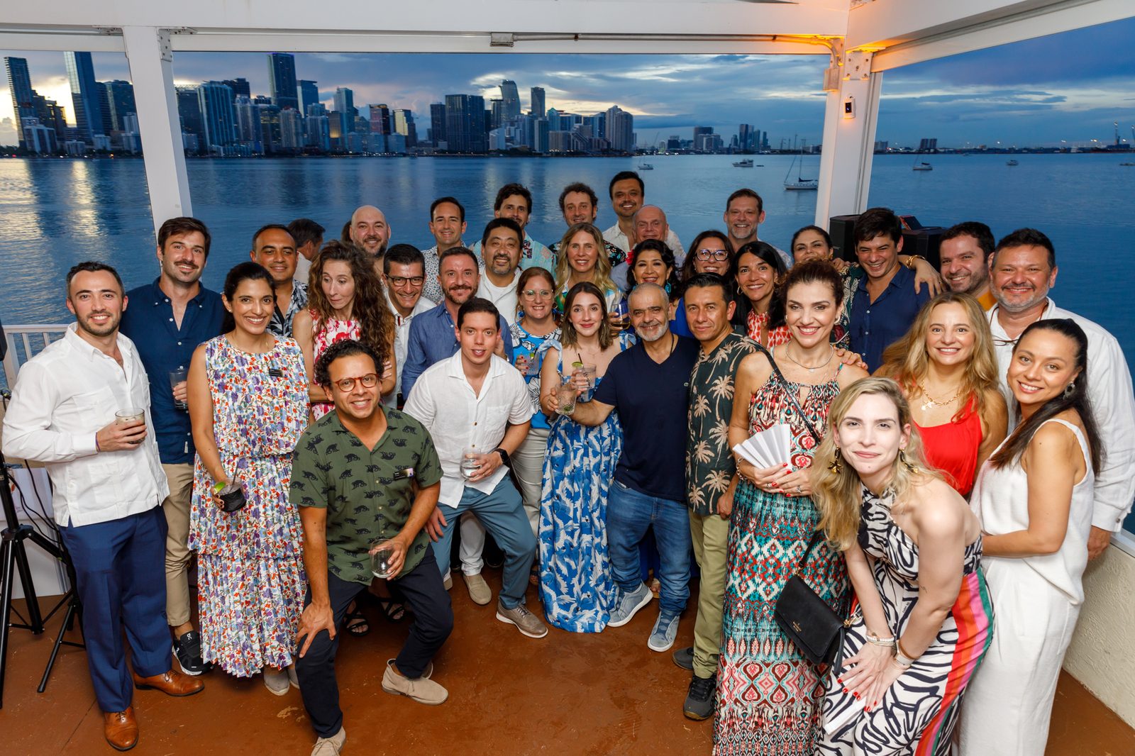Large group of conference attendees posed on a waterfront terrace with the Miami skyline across Biscayne Bay