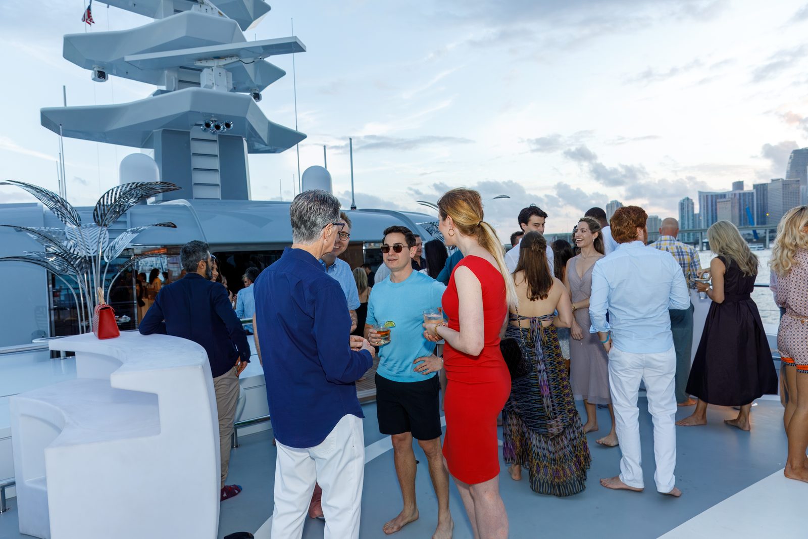 Guests mingling on the upper deck of a yacht at sunset with the downtown Miami skyline in the distance